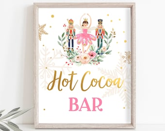 May include: A framed print with a light wood grain frame. The print features a watercolor illustration of a ballerina, two nutcrackers, and floral elements. The words "Hot Cocoa Bar" are in gold script, with "BAR" in pink.