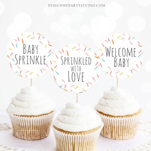 Peut inclure: Trois cupcakes avec un glaçage blanc et des décorations de cupcakes sur le thème des pépites colorées. Les décorations disent "Baby Sprinkle", "Sprinkled with Love" et "Welcome Baby".
