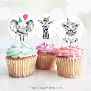 May include: Three cupcake toppers featuring a black and white illustration of an elephant, giraffe, and lion wearing party hats. The toppers are on top of cupcakes with green, pink, and white frosting.