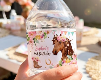 May include: A clear plastic water bottle with a custom label featuring a brown horse, pink and yellow flowers, a cowboy boot, a gold horseshoe, and colourful bunting. The text on the label reads Sophia's 3rd Birthday in a dark script font.