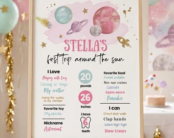 May include: A framed milestone board for a first birthday featuring space-themed watercolor illustrations of planets, stars, and a rocket. The text reads Stella's first trip around the sun, listing personal details like 20 pounds, 26 inches, and 6 teeth.