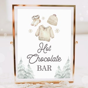 May include: A printable sign for a hot chocolate bar with a watercolour illustration of a jumper, hat, and socks. The sign says "Hot Chocolate Bar" in a grey script font.