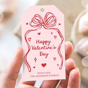 Puede incluir: Etiqueta de regalo rosa con un lazo rojo y el texto "Feliz d&iacute;a de San Valent&iacute;n" y "Con amor, La familia Anderson".