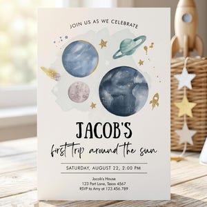 May include: A white rectangular invitation card featuring watercolor space illustrations including planets, a ringed planet, stars, and a rocket. Text reads: JOIN US AS WE CELEBRATE, JACOB'S first trip around the sun, SATURDAY, AUGUST 22, 2:00 PM, Jacob's House, 123 Part Lane, Texas 4567, RSVP to Amy at 123.456.789.