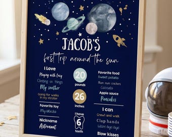 May include: A framed navy blue milestone poster featuring space-themed illustrations of planets, stars, and a rocket. The text reads Jacob's first trip around the sun, listing personal details including 20 pounds, 26 inches, and 6 teeth.