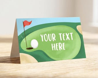 May include: A folded card featuring a golf course illustration with a green putting area, a white golf ball, a red flag, and sand traps. The text "YOUR TEXT HERE" is printed in white on the green area against a light blue sky background.