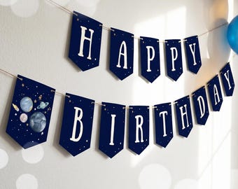 May include: A navy blue birthday banner featuring white lettering that spells out HAPPY BIRTHDAY. The pennant-style flags are decorated with small gold stars and a graphic of planets and a rocket ship on the first flag, all strung on twine.