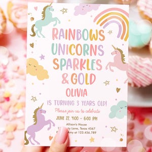 May include: A pastel-themed invitation card featuring unicorns, rainbows, and stars. The text reads "Rainbows, Unicorns, Sparkles & Gold" and "Olivia is turning 3 years old!" The card is held by a person.