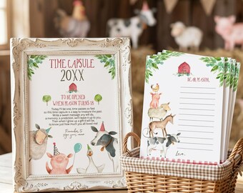 May include: A white ornate frame containing a Time Capsule sign with farm animal illustrations and text, next to a wicker basket holding lined stationery cards featuring a red barn and a stack of farm animals, including a pig, sheep, and cow.