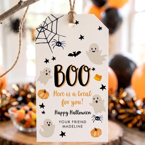 May include: A rectangular white gift tag with rounded top corners, featuring a brown twine loop. The tag displays black and orange text reading BOO, Here is a treat for you!, Happy Halloween, and YOUR FRIEND MADELINE, surrounded by ghosts, pumpkins, spiders, webs, bats, and stars.