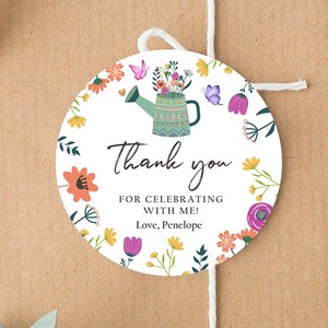 May include: Round thank you tag with a floral design. A green watering can with flowers is in the center. The text reads "Thank you for celebrating with me! Love, Penelope".