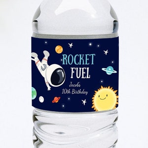 May include: A clear water bottle with a white cap and a label featuring an astronaut, planets, and the words "ROCKET FUEL." The label also includes the text "Jacobs 10th Birthday" in a playful font, perfect for a space-themed party.