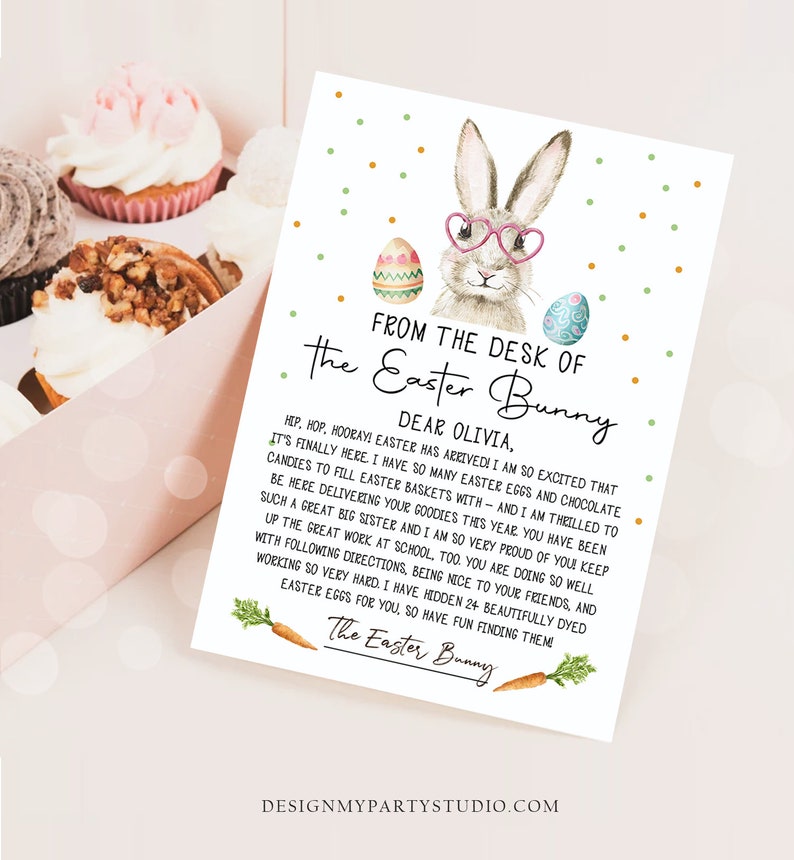 May include: A light blue and green Easter bunny with pink glasses holding a sign that says "From the desk of the Easter Bunny" and a message to Olivia. The sign is decorated with colourful Easter eggs.