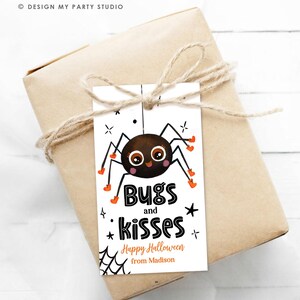 Pu&ograve; includere: Un'etichetta regalo rettangolare bianca con un ragno dei cartoni animati con occhi grandi e stivali arancioni. Il testo recita Bugs and kisses, Happy Halloween e from Madison. L'etichetta &egrave; legata con dello spago a un pacchetto regalo.