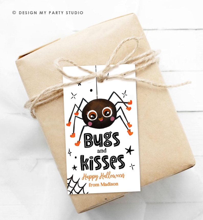 Pu&ograve; includere: Un'etichetta regalo rettangolare bianca con un ragno dei cartoni animati con occhi grandi e stivali arancioni. Il testo recita Bugs and kisses, Happy Halloween e from Madison. L'etichetta &egrave; legata con dello spago a un pacchetto regalo.