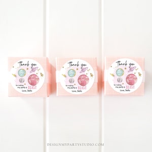 May include: Three pink favor boxes with white circular labels. Each label has a watercolor illustration of planets and stars with gold glitter accents. The text on the labels reads "Thank you for making my party a BLAST Love, Stella."