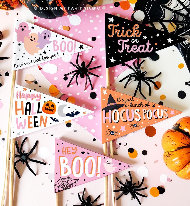 May include: A collection of Halloween-themed pennant flags with various designs and phrases, including "Trick or Treat" and "Hocus Pocus." The flags are in black, orange, and pink, with illustrations of ghosts, spiders, and pumpkins. Black plastic spiders and confetti are scattered around the flags.