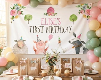 May include: A white birthday backdrop featuring a pink barn, floral accents, and watercolor farm animals including a sheep, pig, goose, and cow. The text reads ELISE'S FIRST BIRTHDAY. Brown paper favor bags and cupcakes are arranged on a wooden table.