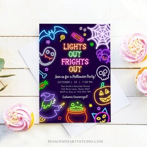 May include: A Halloween party invitation with neon-style illustrations of a bat, ghost, spiderweb, skull, pumpkin, witch, and cat. The invitation reads "LIGHTS OUT FRIGHTS OUT" and includes party details. Two cupcakes with pink frosting are on the right.