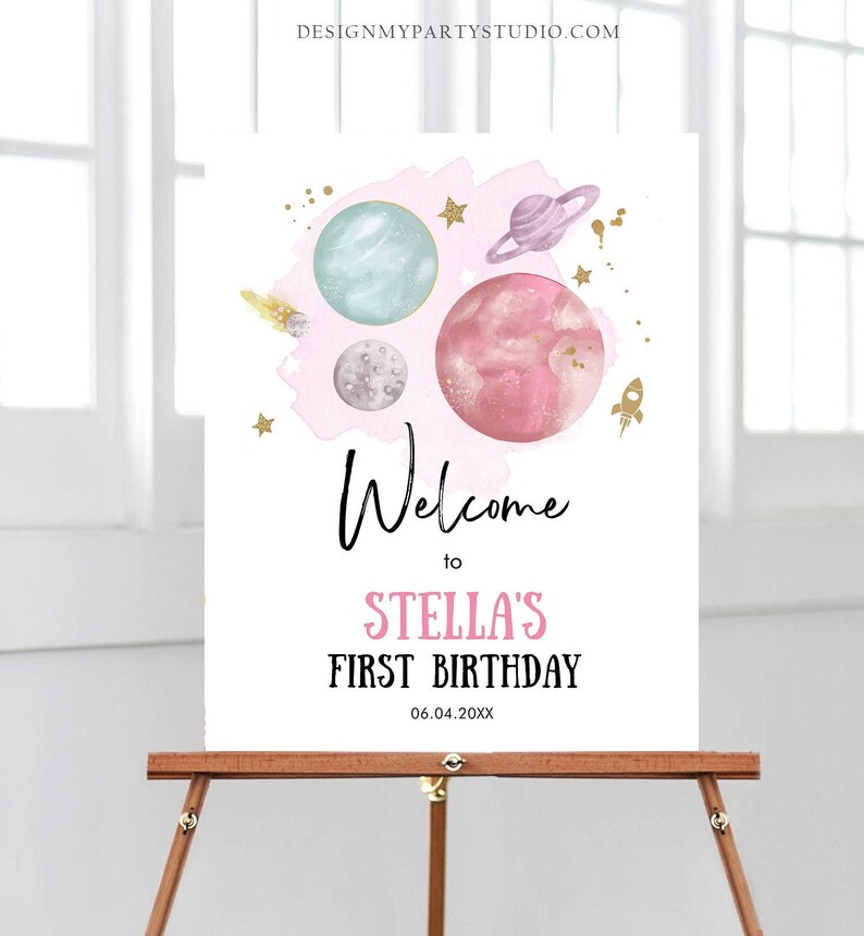 May include: Welcome to Stella's First Birthday sign with a pink watercolor background and gold stars. The sign features a pink, blue, and gray planets with a gold rocket.