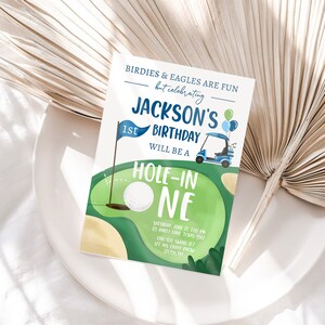 May include: A blue and green golf-themed birthday invitation for a 1st birthday party. The invitation features a golf cart, a golf ball, and the text "Jackson's 1st Birthday Will Be A Hole-In-One".