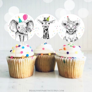May include: Three cupcake toppers featuring a black and white elephant, giraffe, and lion wearing party hats. The toppers are on top of cupcakes with white frosting and colorful sprinkles.