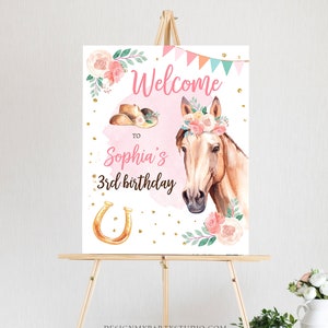 May include: Welcome to Sophia's 3rd birthday party sign with a pink background, a horse with a floral crown, a cowboy hat, a horseshoe, and gold glitter.