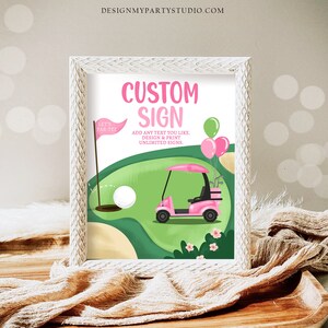 May include: A pink and green golf cart with balloons on a green golf course. The text "CUSTOM SIGN" is in pink letters. The text "ADD ANY TEXT YOU LIKE, DESIGN & PRINT UNLIMITED SIGNS." is in black letters.