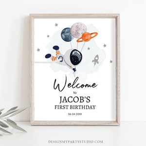 Op de afbeelding: Een afdrukbaar welkomsbord voor een eerste verjaardag met een cartoon-astronaut die ballonnen in de vorm van planeten vasthoudt. Het bord zegt "Welkom bij Jacob's First Birthday 06.04.20XX".