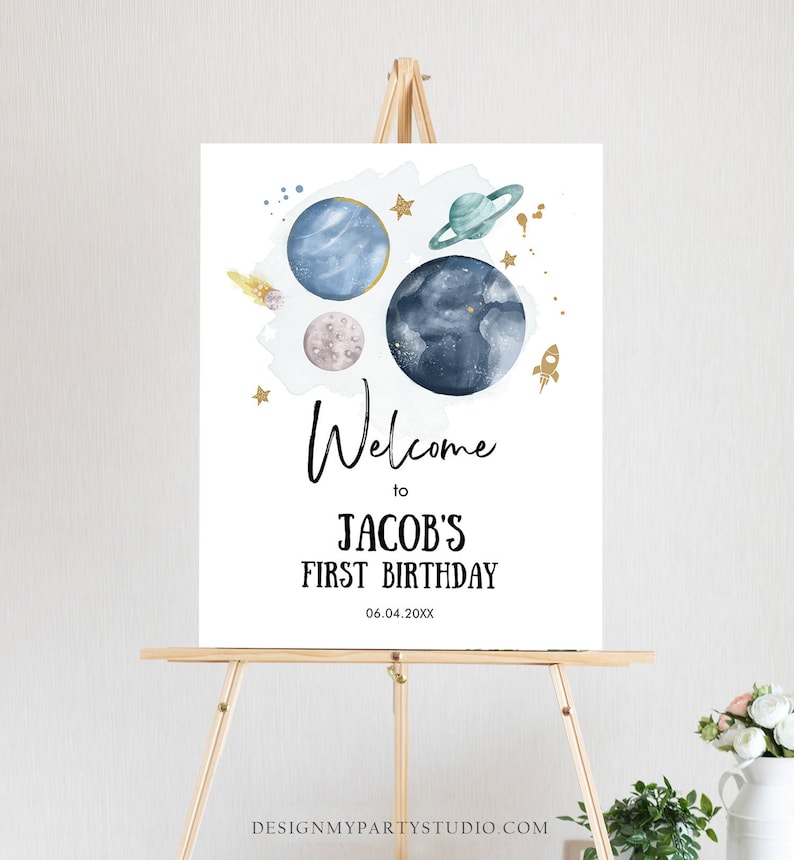 May include: Welcome to Jacob's First Birthday sign with a blue, white, and gold space theme. The sign features planets, stars, and a rocket ship.