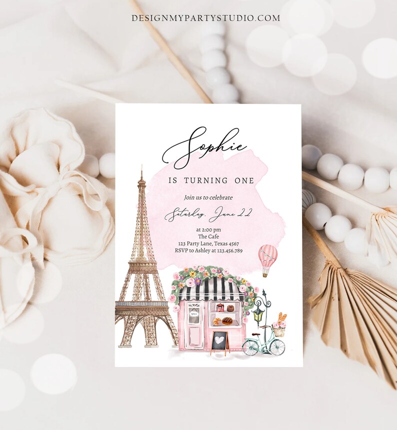 Pode incluir: Um convite de anivers&aacute;rio rosa e branco com fundo aquarela. O convite apresenta um desenho da Torre Eiffel, um caf&eacute; parisiense e um bal&atilde;o de ar quente. O texto do convite diz: "Sophie est&aacute; completando um ano. Junte-se a n&oacute;s para celebrar S&aacute;bado, 22 de junho &agrave;s 14:00 The Cafe 123 Party Lane, Texas 4567 RSVP para Ashley no 123.456.789"