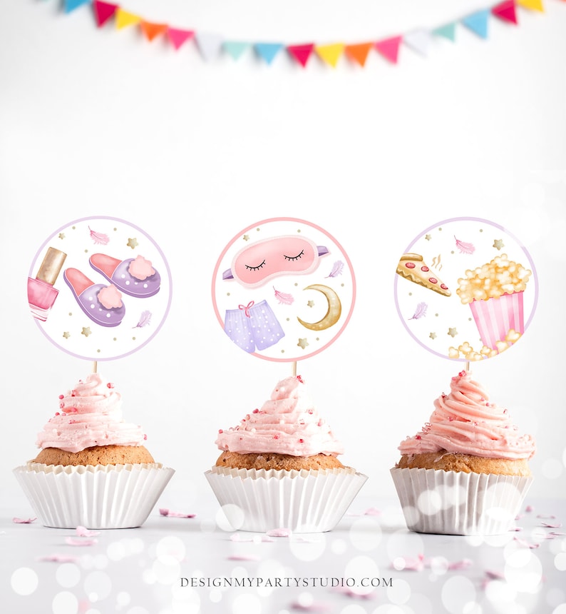 May include: Three cupcake toppers with a sleepover theme. The toppers are round and feature illustrations of a sleep mask, slippers, nail polish, popcorn, and pizza. The toppers are on top of cupcakes with pink frosting.