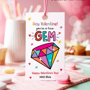 May include: A white card with a pink string attached to the top. The card has a colourful diamond with sparkles and the text "Hey Valentine! You're a true GEM" and "Happy Valentine's Day! XOXO Olivia".