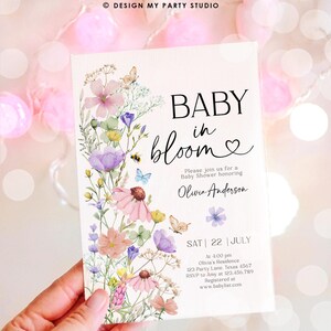 May include: A baby shower invitation with a watercolor floral design. The text reads "Baby in Bloom" with a heart and "Please join us for a Baby Shower honoring Olivia Anderson". The invitation includes the date, time, location, RSVP information, and website for the baby shower.