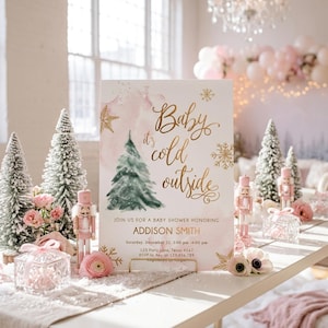 May include: A rectangular baby shower invitation sign featuring a watercolour pink background, a green pine tree illustration, and gold foil text that reads Baby it's cold outside, JOIN US FOR A BABY SHOWER HONORING ADDISON SMITH, Saturday, December 22, 3:00 pm - 4:00 pm, 123 Party Lane, Texas 4567, RSVP to Amy at 123.456.789.