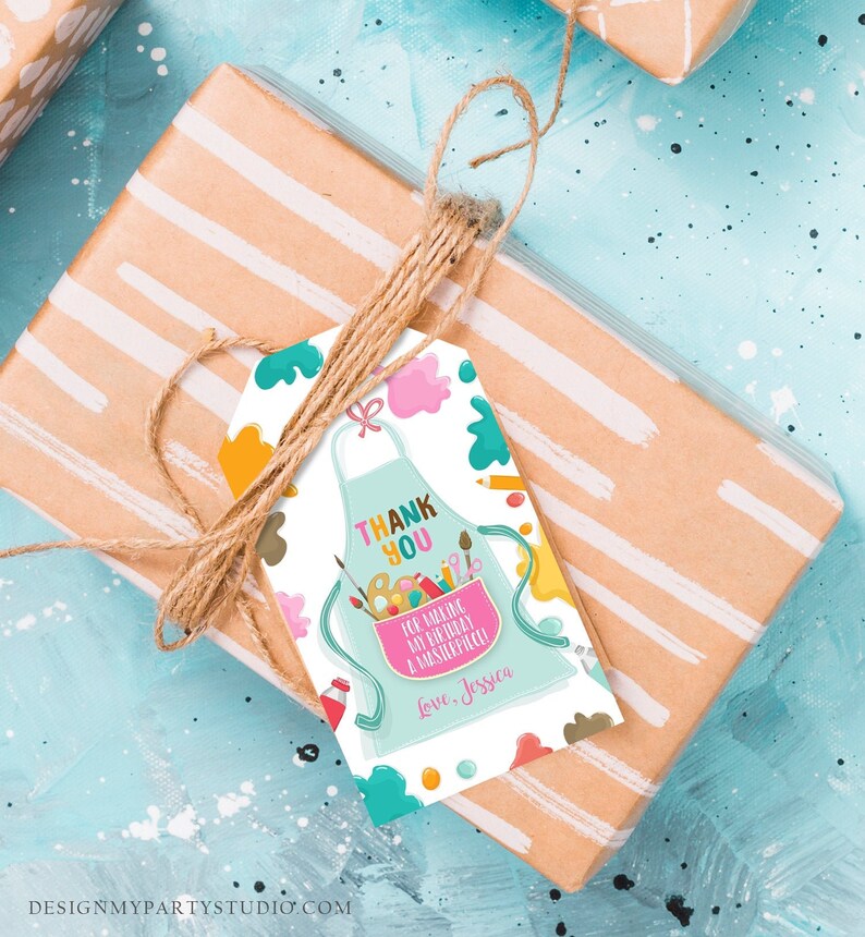 May include: A gift tag with a light blue apron design, featuring the text "THANK YOU" and "FOR MAKING MY BIRTHDAY A MASTERPIECE!" with the name "Jessica". The tag is tied with twine to a wrapped gift with white stripes.