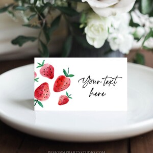 May include: White place card with a watercolor design of red strawberries. The text "Your text here" is written in black cursive.
