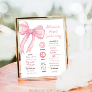 May include: Pink and white first birthday milestone poster with a large pink bow at the top. The poster lists the child's age, weight, height, and other milestones. The text on the poster reads "Allison's First Birthday".