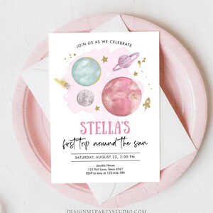 May include: A pink and blue space-themed invitation for a first birthday party. The invitation features planets, stars, and a rocket ship. The text on the invitation reads "Stella's first trip around the sun." The invitation also includes the date, time, and location of the party.