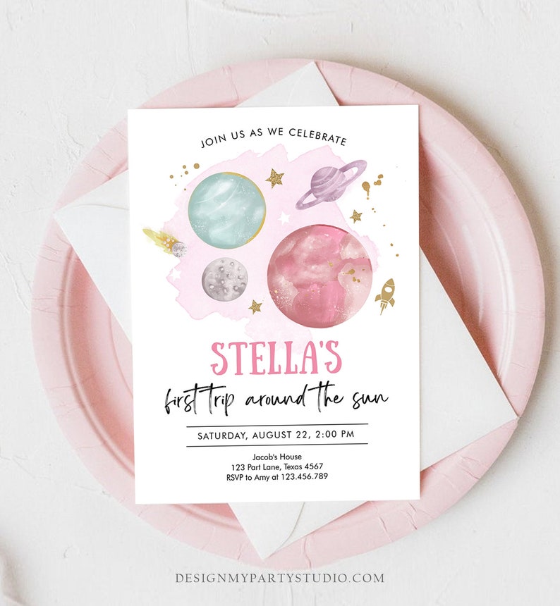 May include: A pink and blue space-themed invitation for a first birthday party. The invitation features planets, stars, and a rocket ship. The text on the invitation reads "Stella's first trip around the sun." The invitation also includes the date, time, and location of the party.