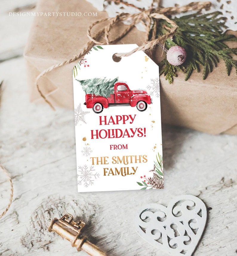 Puede incluir: Una etiqueta de regalo blanca con un cami&oacute;n rojo que transporta un &aacute;rbol de Navidad. La etiqueta dice "Happy Holidays!" y "From The Smith's Family" en letras rojas y doradas. Copos de nieve y vegetaci&oacute;n decoran los bordes.