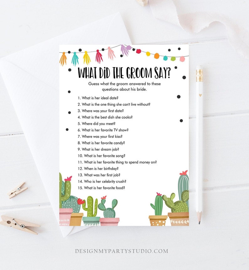 May include: A white card with the text "WHAT DID THE GROOM SAY?" and a list of questions about the bride. The card is decorated with colorful string lights and cactus illustrations. A pencil and clothespins are also visible.