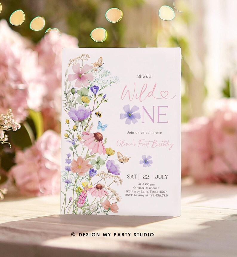 May include: A floral-themed first birthday invitation with a watercolor design. The invitation features a pink and purple floral arrangement with butterflies and bees. The text reads "She's a Wild One" and includes details for the party, including the date, time, and location. The invitation is designed by "Design My Party Studio."