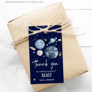 May include: A blue thank you tag with a space theme. It features planets, stars, and a rocket ship. The text reads "Thank you for making my party a BLAST. Love, Jackson."