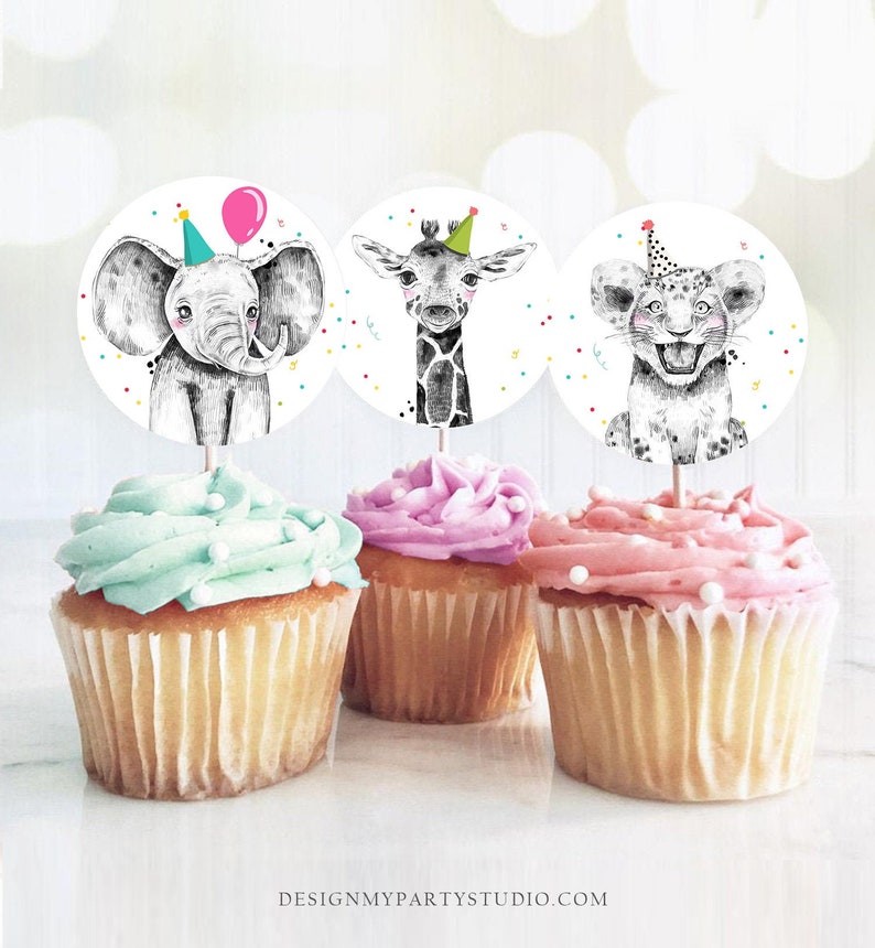 May include: Three cupcake toppers featuring a black and white illustration of an elephant, giraffe, and lion wearing party hats. The toppers are on top of cupcakes with green, pink, and white frosting.