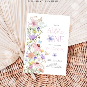 May include: A floral-themed first birthday party invitation with a watercolor design featuring pink, purple, and yellow flowers. The text reads "She's a Wilde One" and includes details for the party, including the date, time, location, and RSVP information.