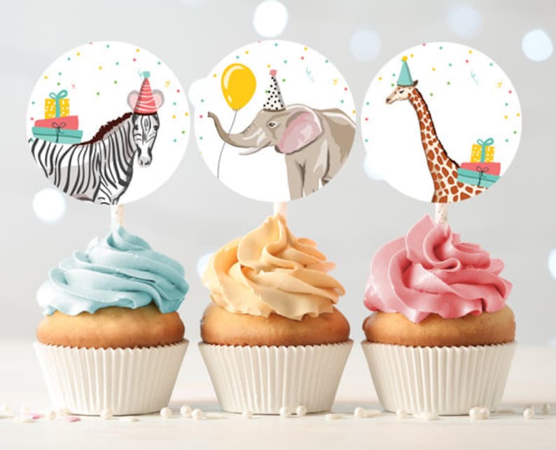 May include: Three cupcake toppers featuring a zebra, elephant, and giraffe. Each topper has a colorful party hat and a gift box. The toppers are on top of cupcakes with blue, yellow, and pink frosting.