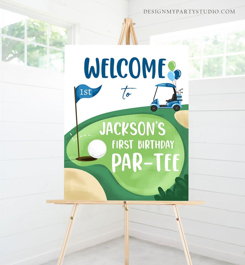 May include: Welcome to Jackson's 1st Birthday Par-Tee sign with a green golf course, a golf cart, a golf ball, and blue and green balloons.