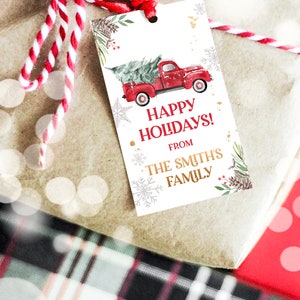 Puede incluir: Una etiqueta de regalo con un cami&oacute;n rojo vintage que transporta un &aacute;rbol de Navidad. La etiqueta dice "Happy Holidays! From The Smith's Family" con detalles de copos de nieve y pino. La etiqueta est&aacute; atada a un regalo envuelto.