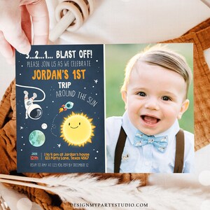 May include: A blue and orange space-themed first birthday party invitation with a photo of a baby boy wearing a bow tie. The invitation says "3...2...1... BLAST OFF! Please join us as we celebrate Jordan's 1st Trip Around the Sun" and includes the date, time, and location of the party.